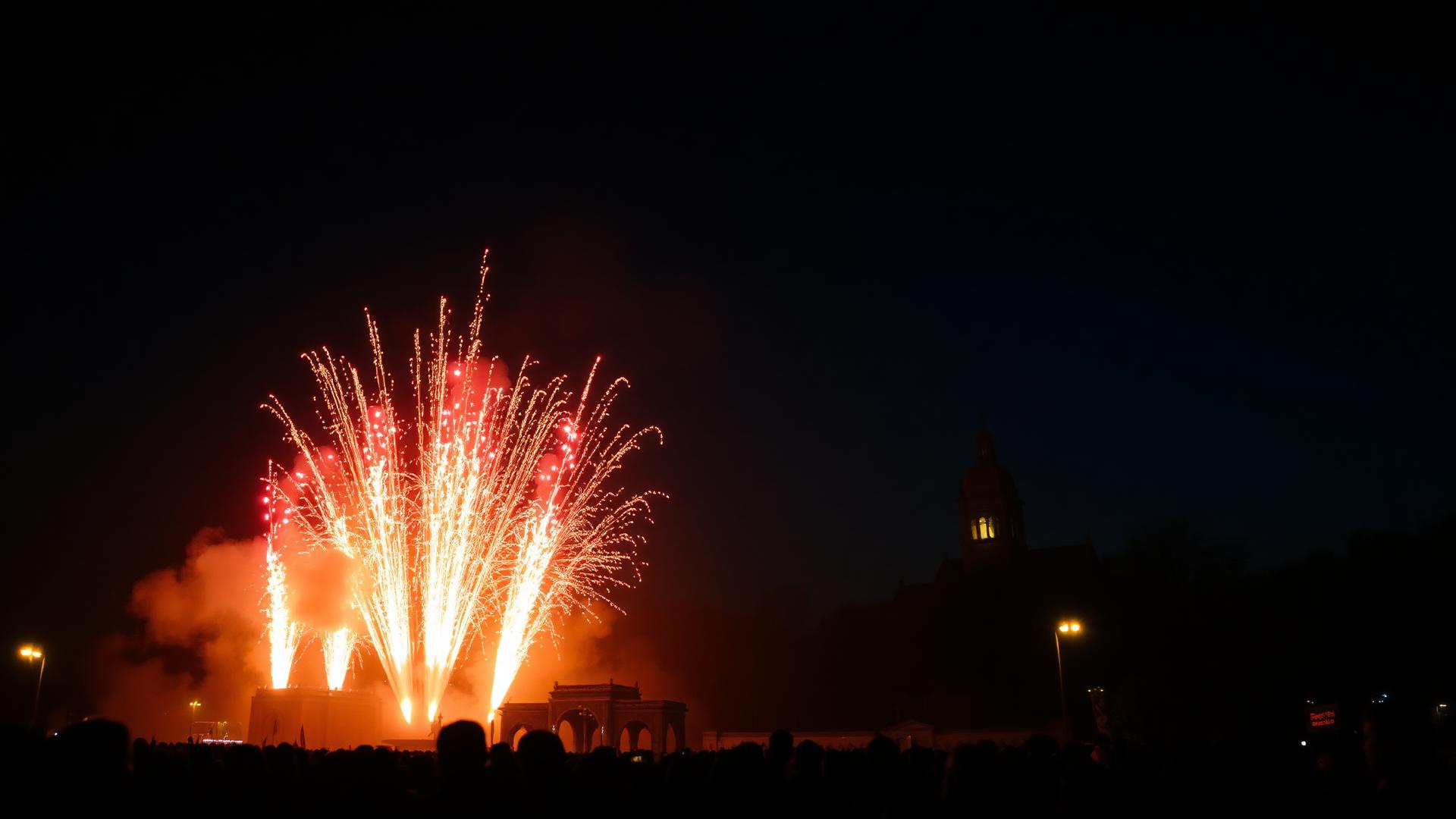 Pyroscénie nocturne : gerbes de feu s'élevant devant un monument, foule silhouettée émerveillée